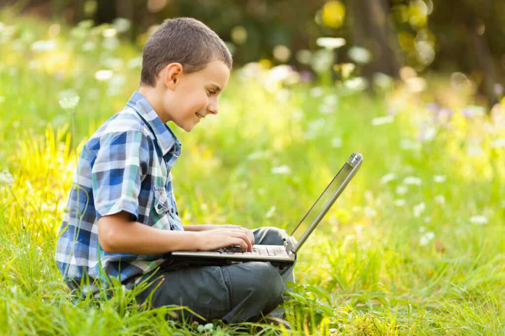 An unschooling student using a laptop to research while sitting outside