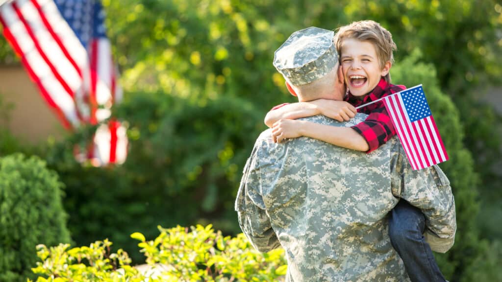 A smiling homeschool child being held by a military parent