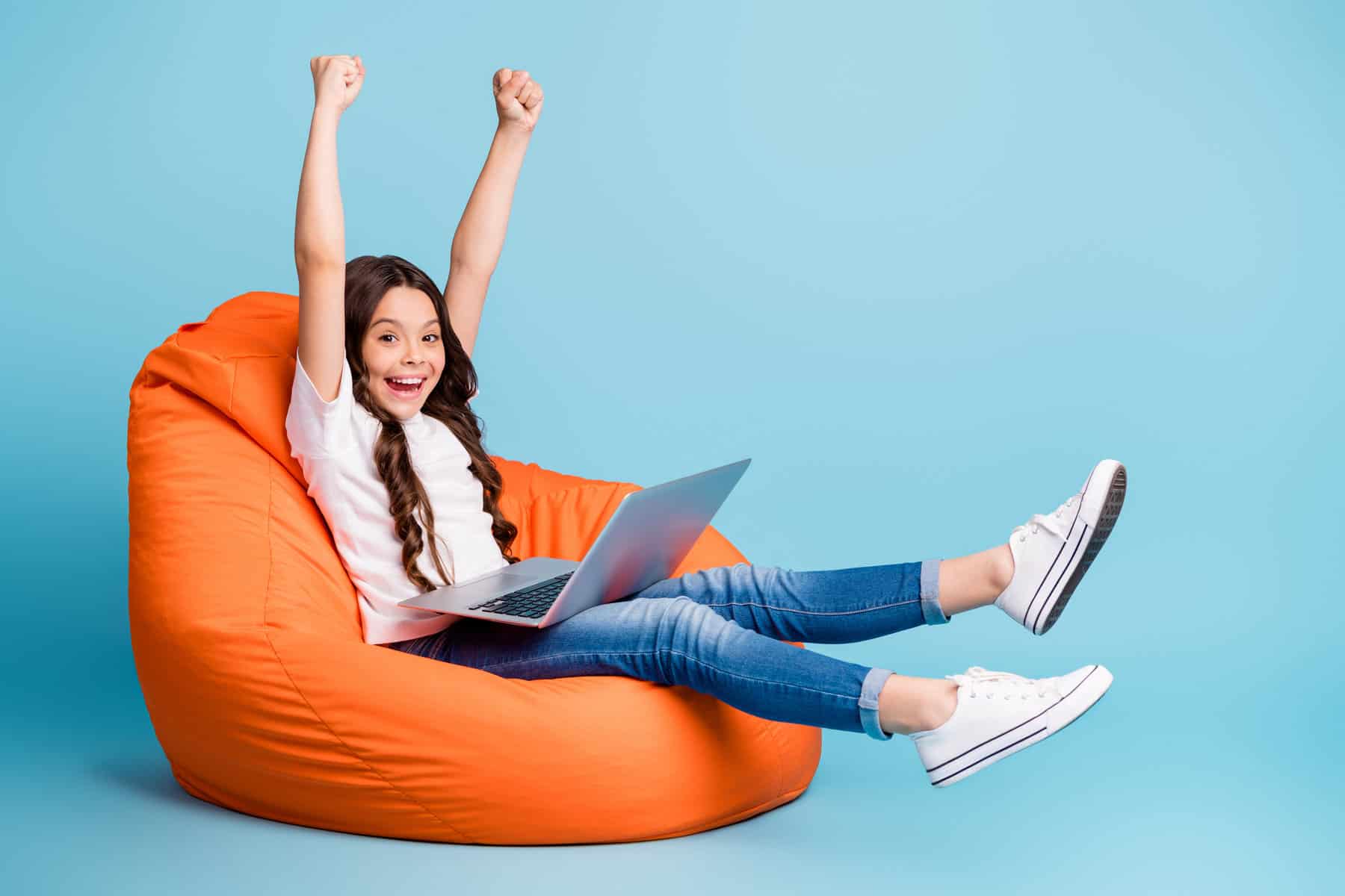 Young girl sitting on an orange beanbag using a laptop