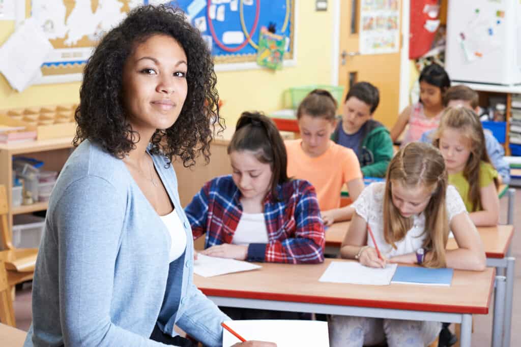 Portrait of a teacher in her classroom with young students working
