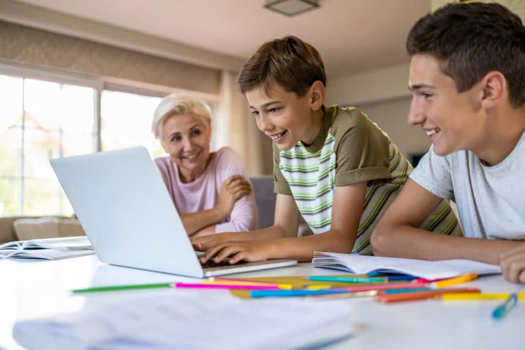 Two young boys working on a laptop while their grandmother watches