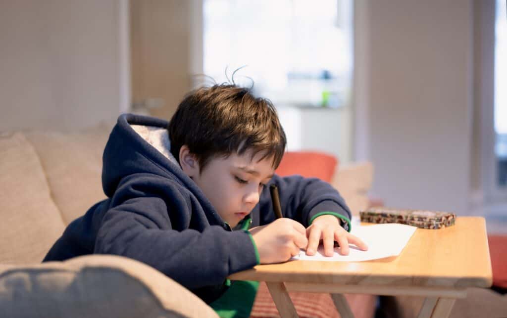 Little boy in a winter coat writing with a crayon