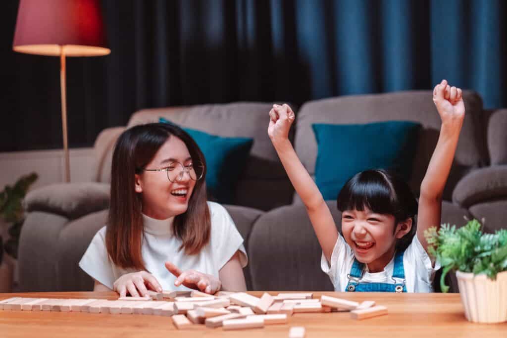 Two young Asian girls play a board game together at the table