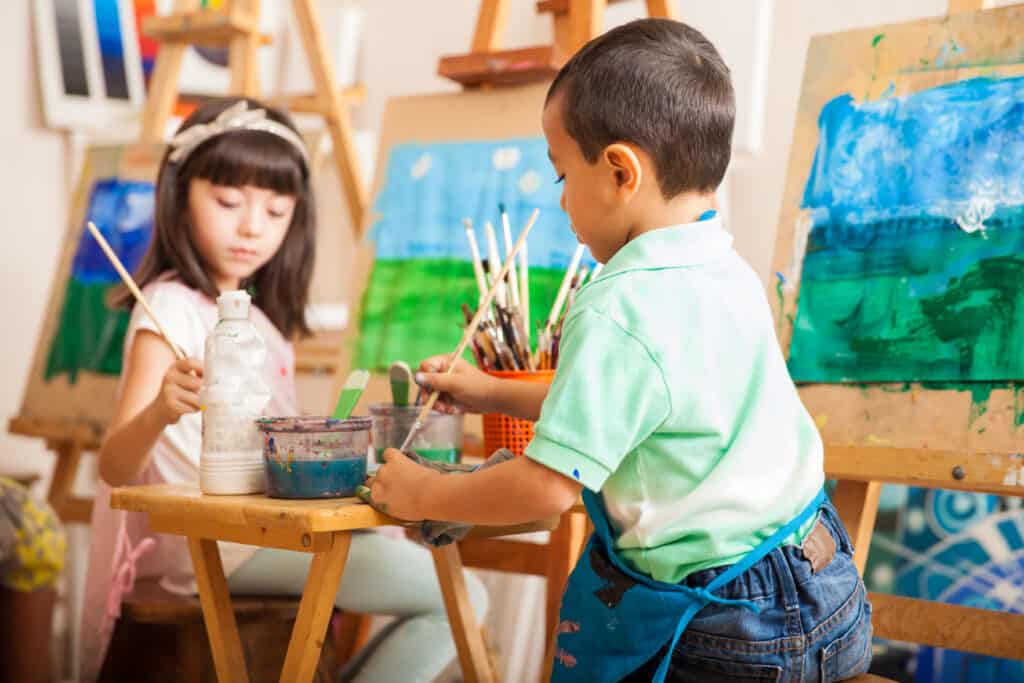 Two kids using easels to paint a landscape
