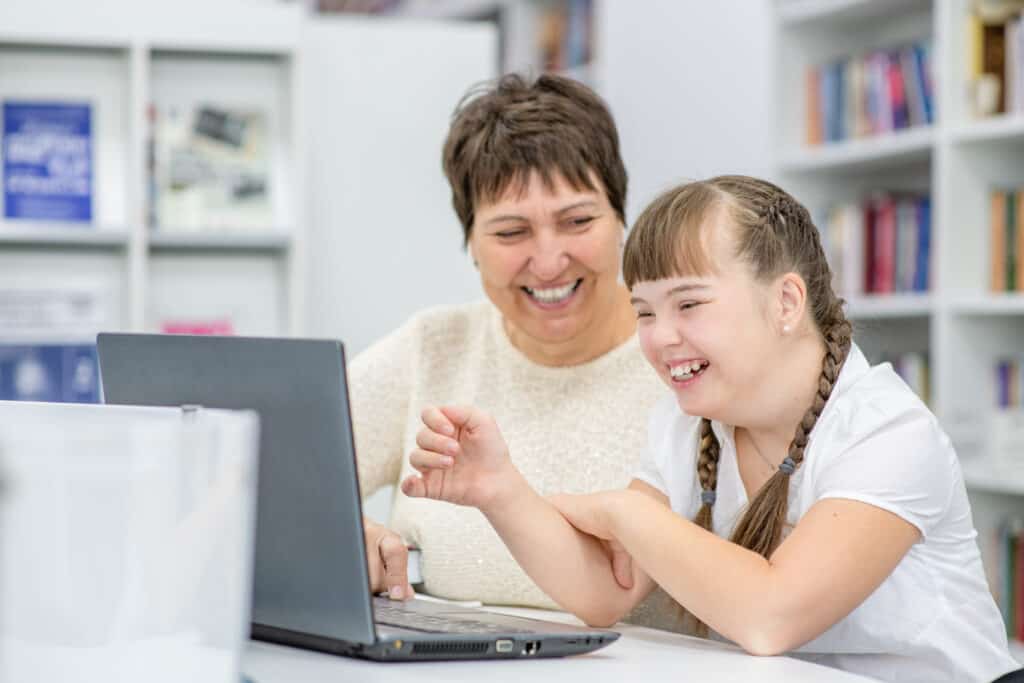 Parent helping daughter with down syndrome use the computer