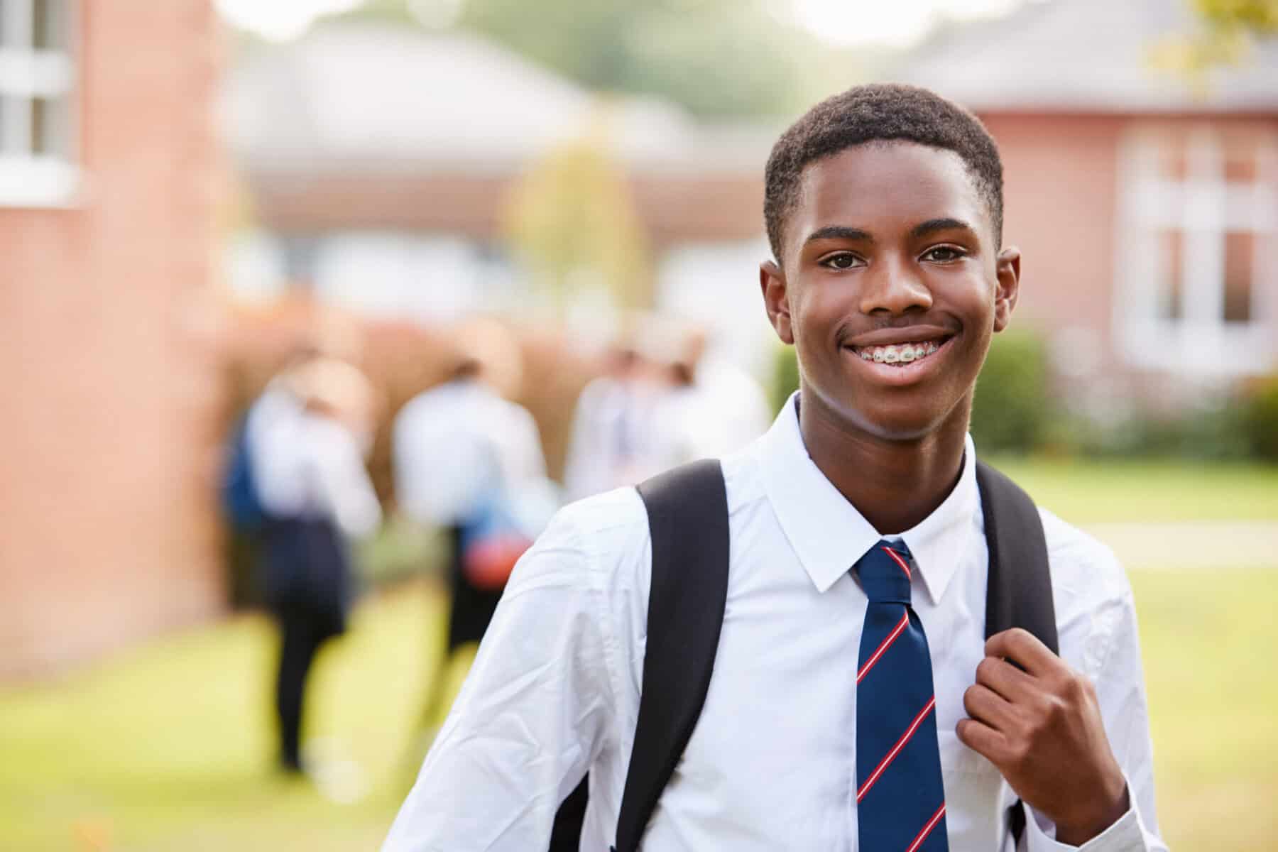 Private school teen boy with braces smiling and holding a backpack