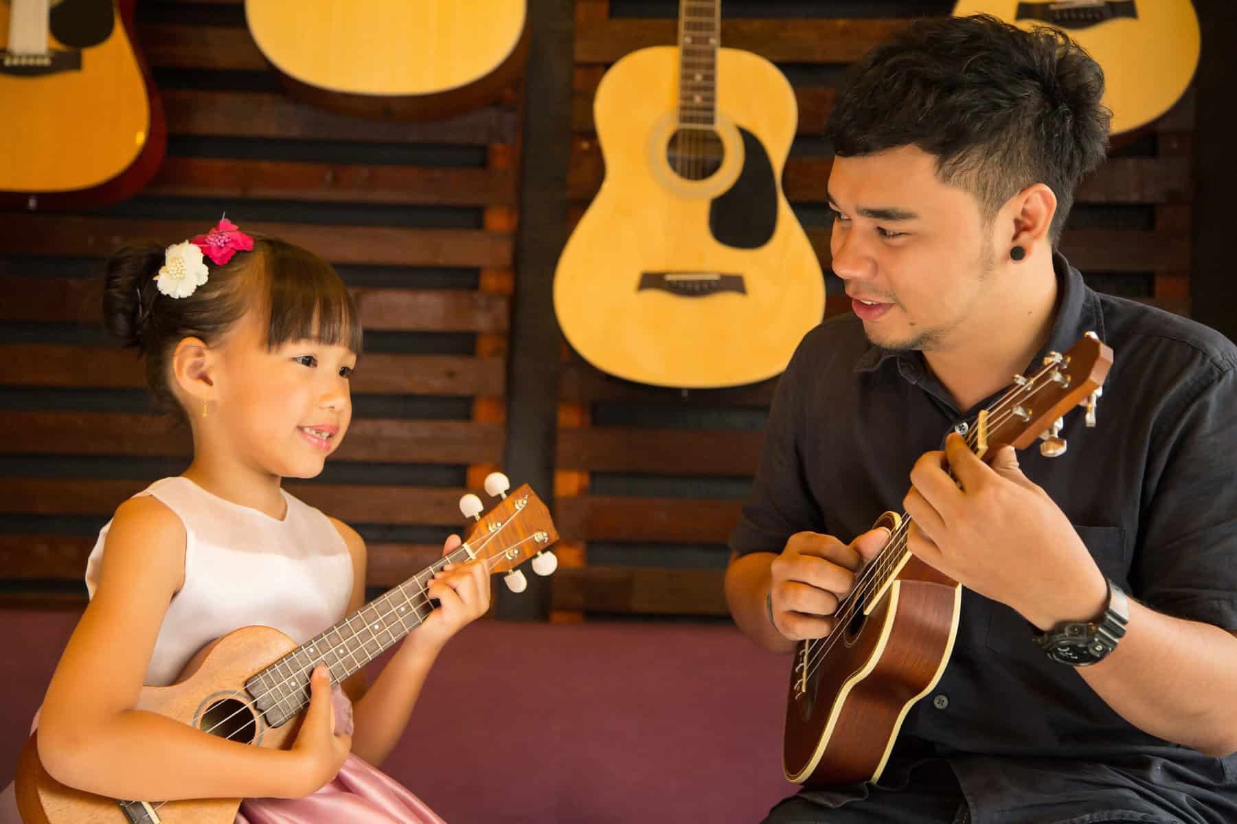 Man teaching young girl how to play ukulele